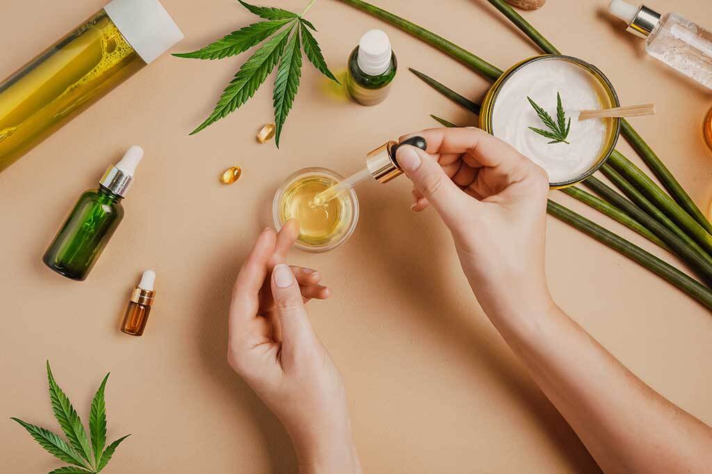 CBD oil in female hands on a table background with cosmetics, cream with cannabis and hemp leaves